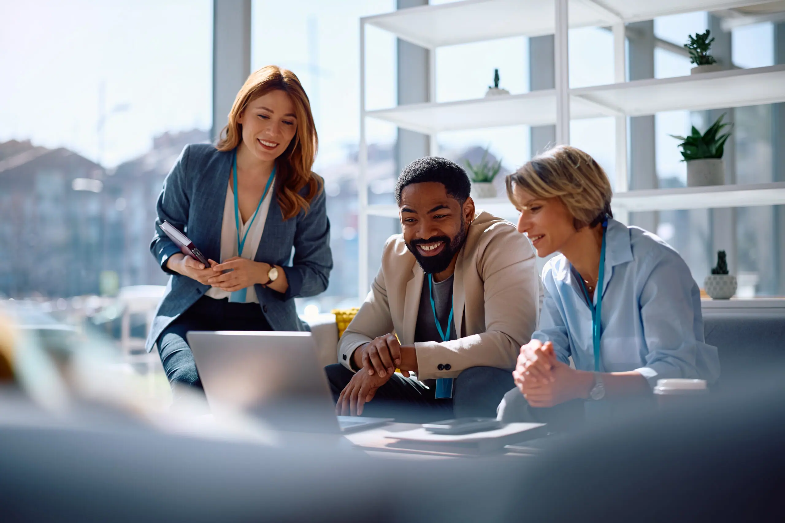 Three colleagues laughing together over a laptop in a meeting