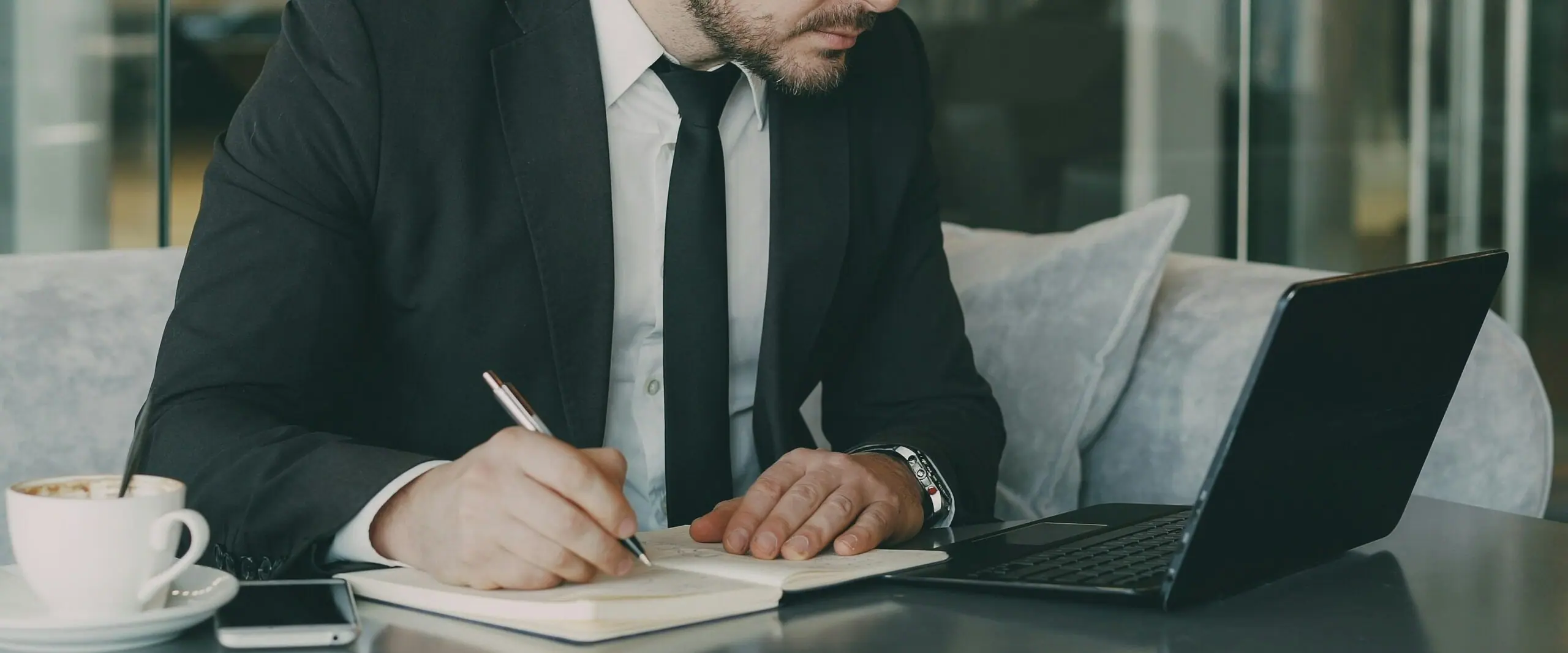 Businessman writing in a notebook beside a laptop