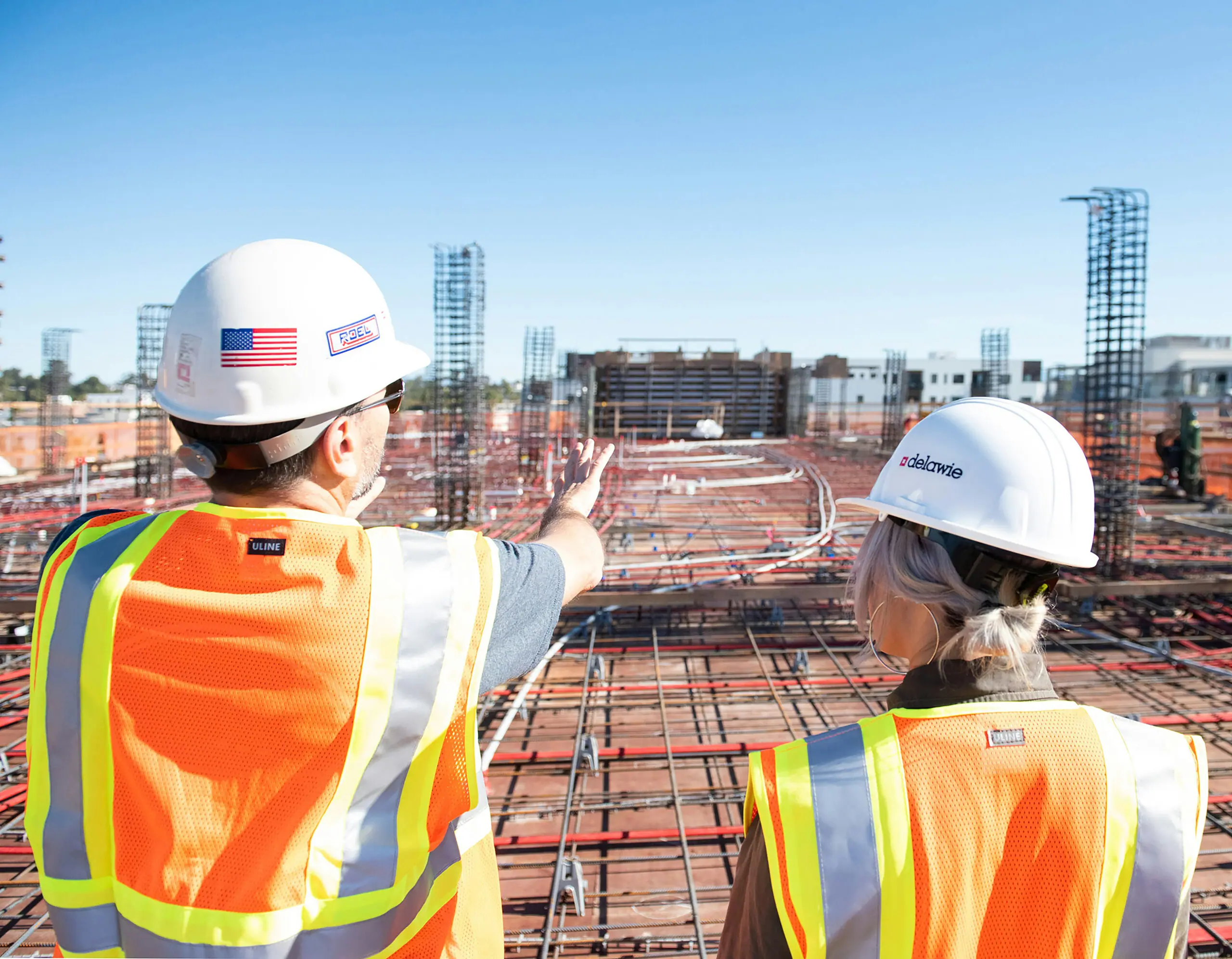 Two site managers in hard hats and safety vests reviewing a construction site