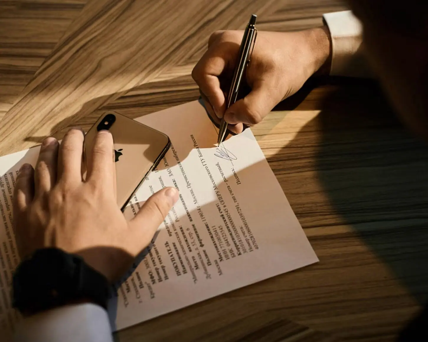 Hands signing an engagement agreement on a wooden desk