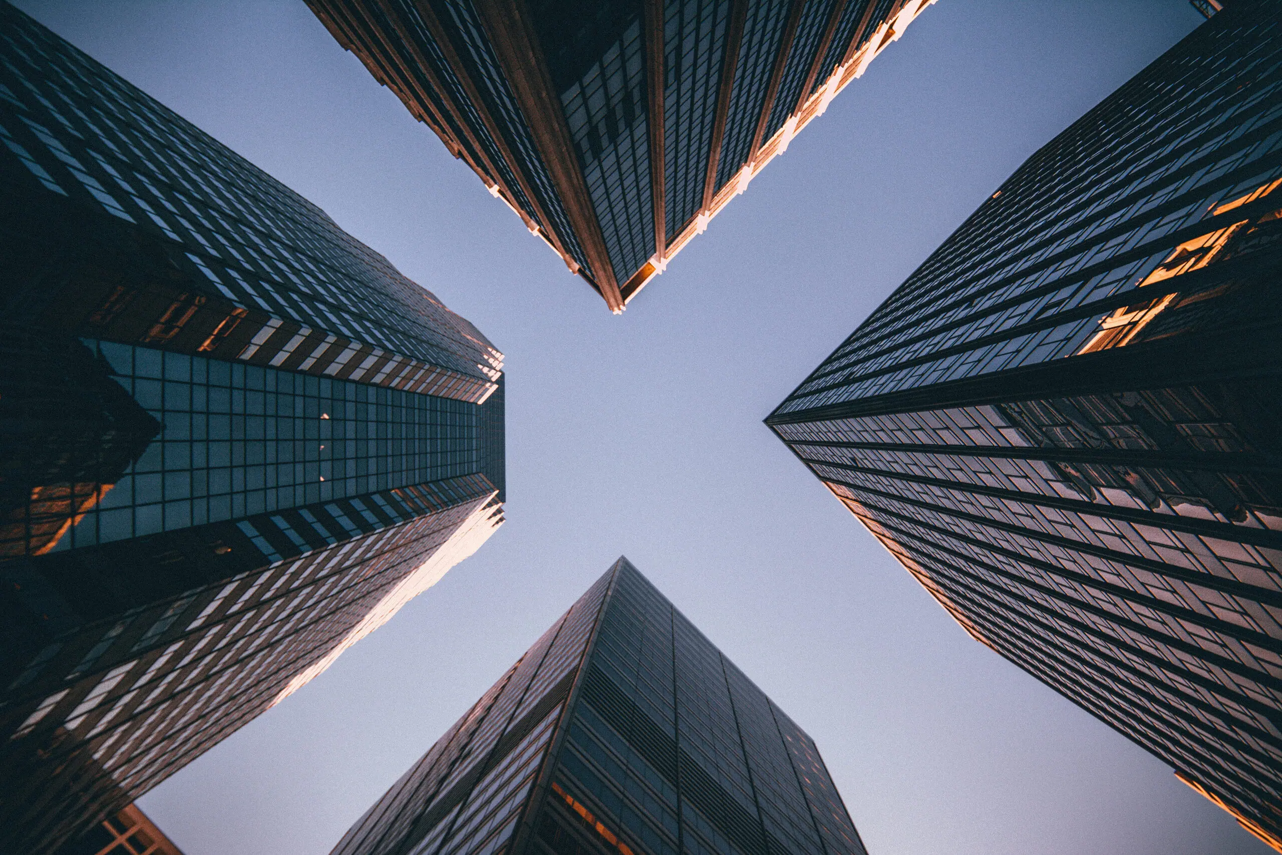Looking up between glass skyscrapers against a clear sky